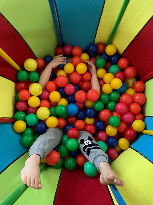 A child happily playing in a colorful ball pit, only their arms and legs are visible as they are almost buried in the balls.