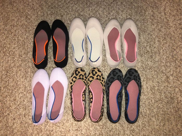 Eight pairs of flats displayed on a beige carpet, showcasing various designs, including solid colors, black, white, and leopard print patterns.