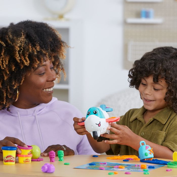 A woman and her child joyfully playing with Play-Doh toys and a toy airplane at a table, sharing smiles together
