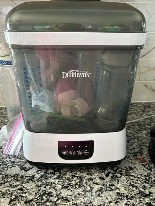 Dr. Brown's baby bottle sterilizer sitting on a kitchen counter, filled with baby bottles and accessories
