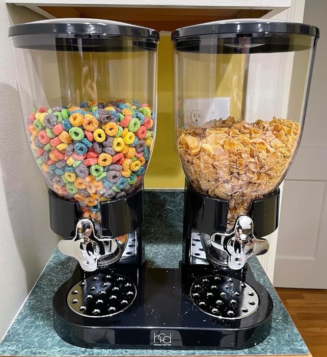 two cereal dispensers on a kitchen counter, one filled with colorful loop cereal and the other with cornflakes, featuring silver levers for easy dispensing