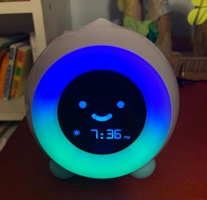 a kid-friendly digital clock with a smiling face display showing 7:36 PM, surrounded by a soft glowing light