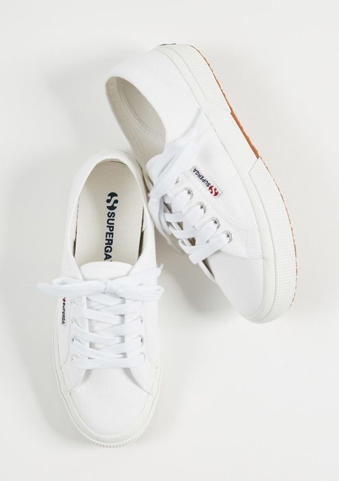 Pair of white sneakers featuring white laces and rubber soles, displayed against a white background.