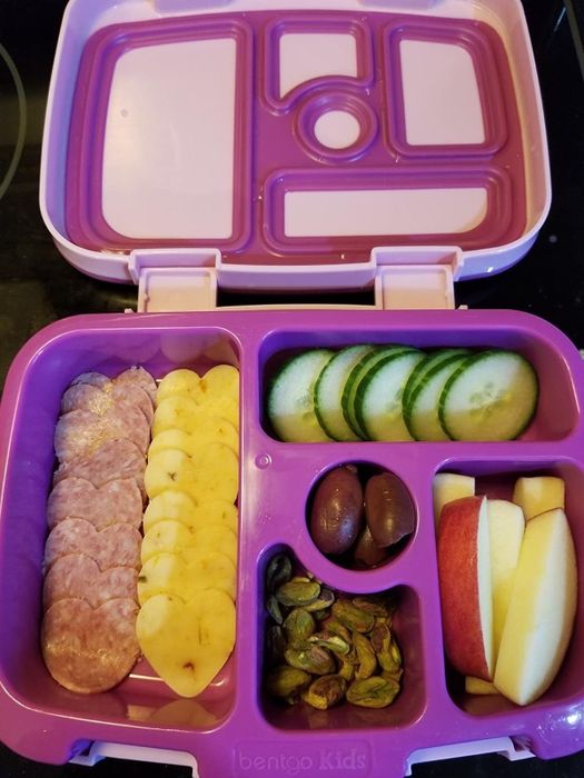 a purple lunchbox containing heart-shaped meat and cheese slices, cucumbers, apple slices, olives, and nuts