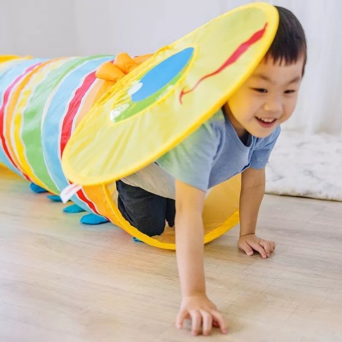 A child grinning as they crawl through a colorful play tunnel in a playroom.