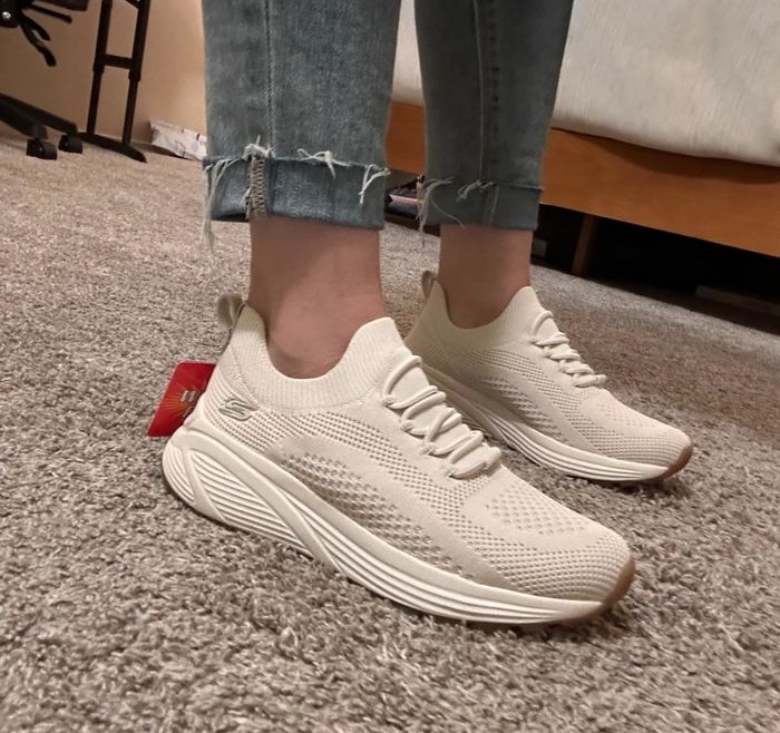 A reviewer wears slip-on sneakers in beige, designed with a thick sole and faux laces, offering both comfort and a stylish look.