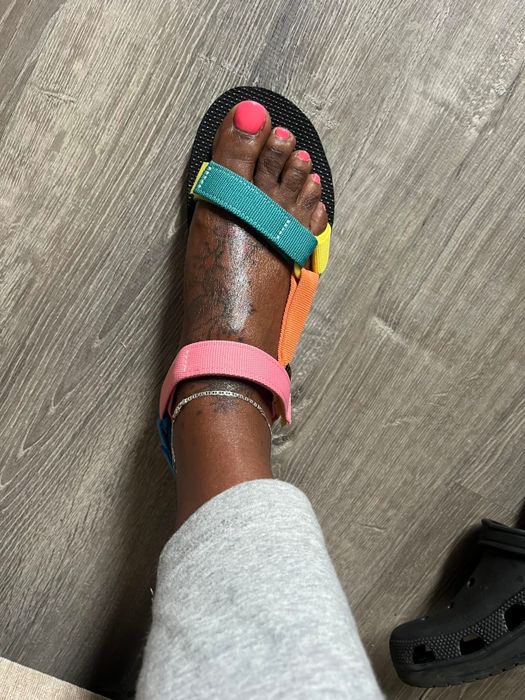 Reviewer wearing the sandals in green, yellow, orange, and pink, matched with grey sweatpants.