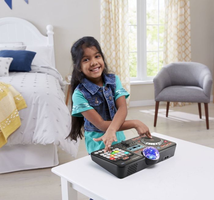 A young girl grinning while interacting with a DJ toy on a white table in a cozy bedroom.
