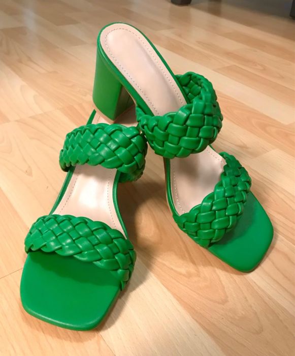 A pair of green braided high-heeled sandals resting on a wooden floor.