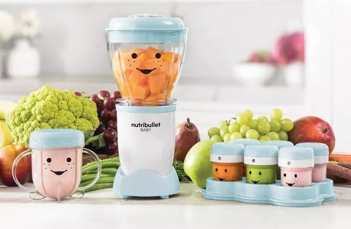A NutriBullet Baby food blender with cheerful containers displayed on a counter alongside assorted fruits and vegetables, promoting a healthy eating lifestyle