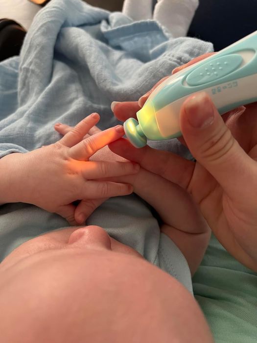 A close-up of a hand gently using an electric nail file on a baby's tiny fingers