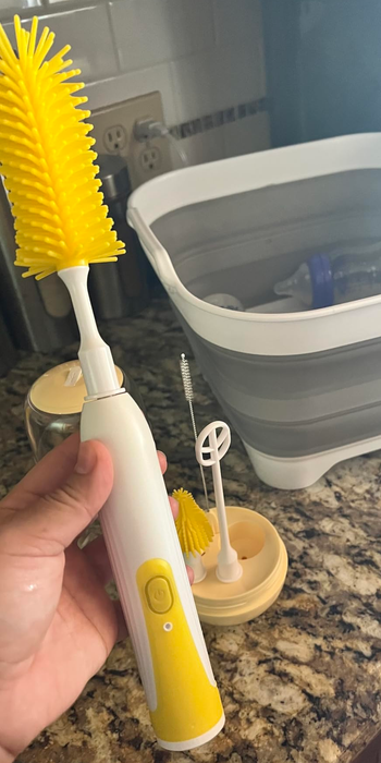A reviewer demonstrating an electric baby bottle scrubber with a bottle washer