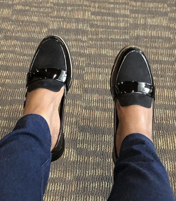 A person modeling the shoes in a glossy black patent leather finish.