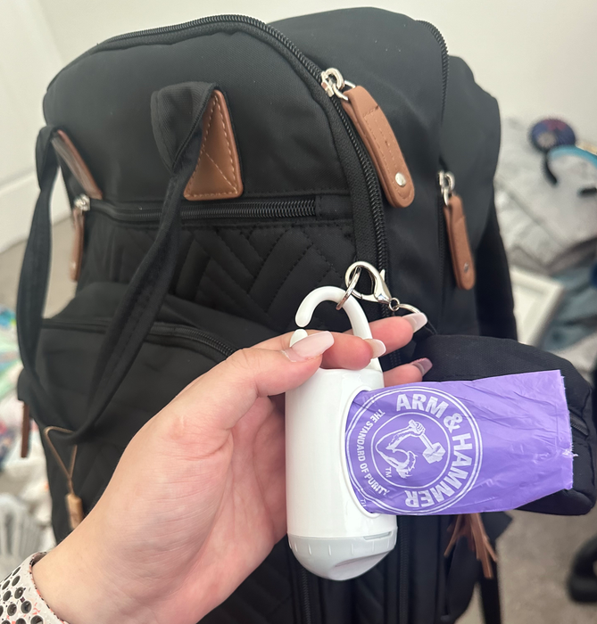 A writer holding a roll of Arm & Hammer lavender-scented bags clipped onto a stylish black and brown quilted diaper bag