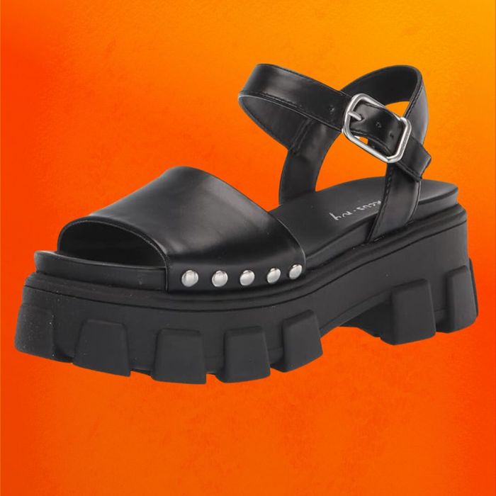 Chunky black sandals with an ankle strap, displayed on an orange background