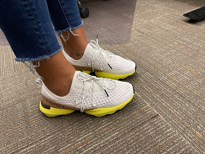 a reviewer showcasing white sneakers featuring tan and yellow highlights