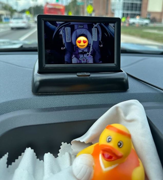 A photo of a car dashboard featuring a digital device showing a cartoon character, with a rubber duck placed in the foreground