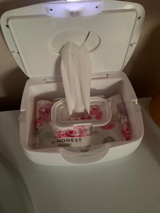 An open white wipe dispenser displaying a pack of Honest baby wipes inside