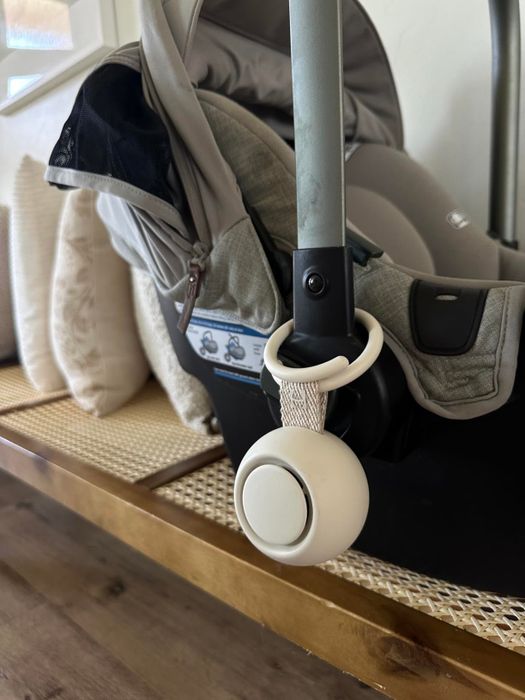 A close-up view of a baby car seat handle with a white noise machine attached
