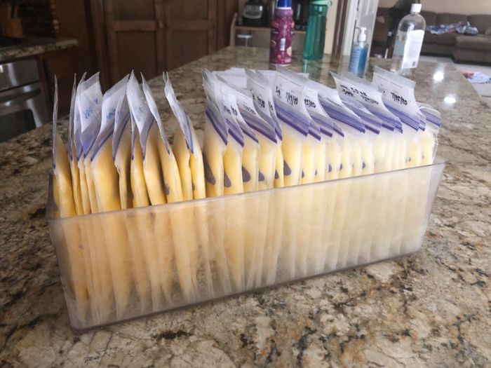 A clear container filled with neatly organized sealed bags of frozen breast milk