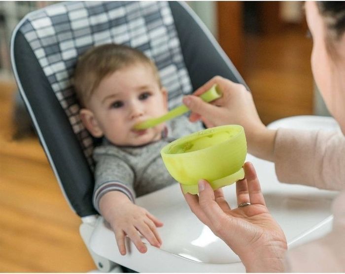 A parent feeding a baby using a spoon and bowl set