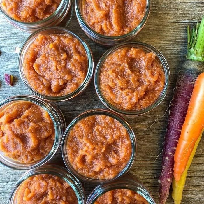 Jars of carrot baby puree displayed on a wooden table alongside fresh carrots