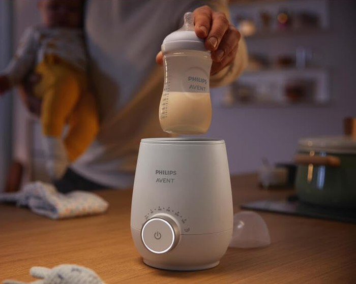 A model demonstrates using a Philips Avent baby bottle with a Philips Avent bottle warmer