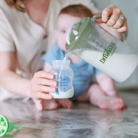 An adult pouring formula into a bottle using a mixing pitcher