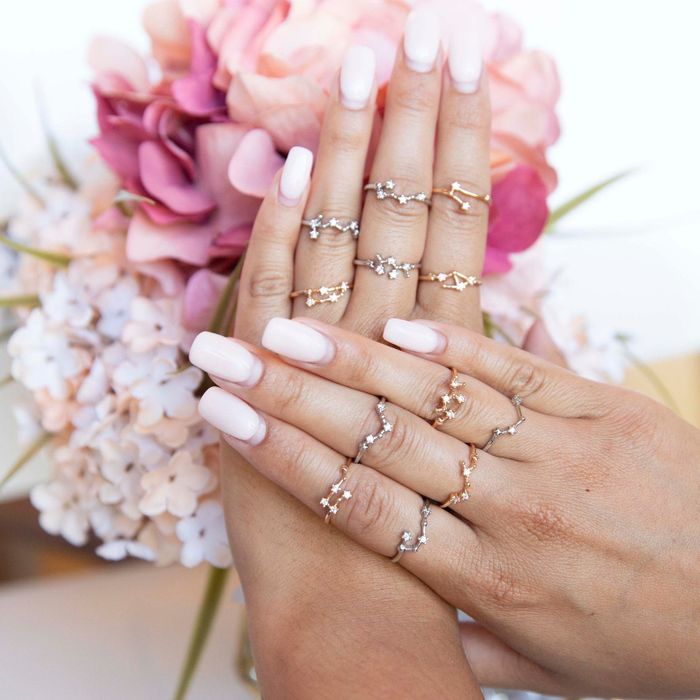 A model’s hands adorned with a variety of zodiac sign rings in both gold and silver, one on each finger.