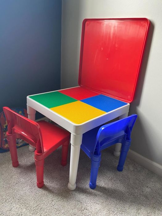 A child's building block table with surfaces in red, green, blue, and yellow, accompanied by a red chair and a blue chair.