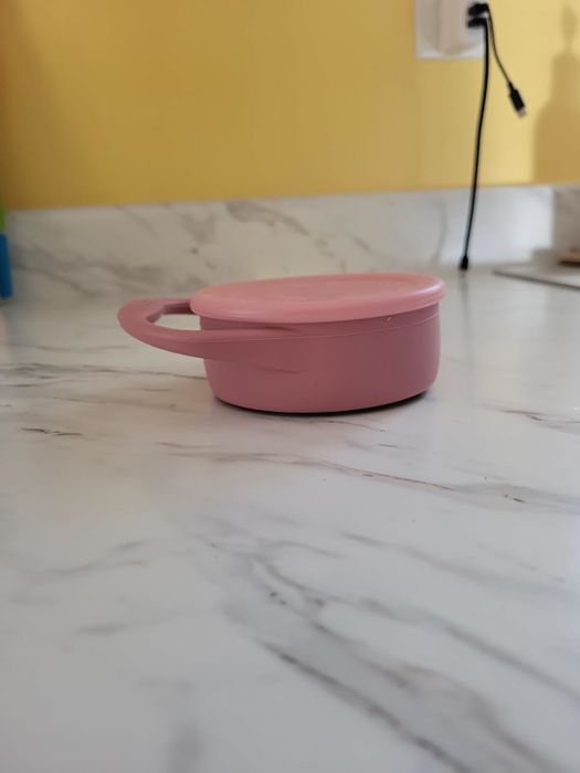 A circular pink container featuring a handle, placed on a marble countertop, ideal for organizing small belongings