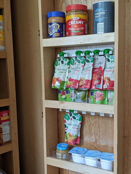 The pantry shelves are neatly arranged with Beech-Nut baby food pouches, jars of peanut butter, iodized salt, and assorted condiment packets.