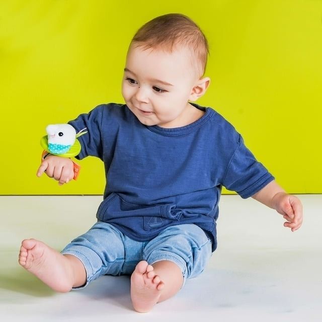 A baby dressed casually playing with a rattle secured to its wrist