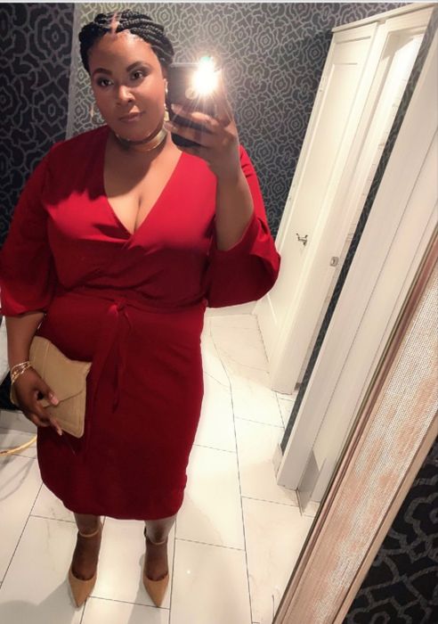 a reviewer posing in a red dress with a tan handbag, capturing a mirror selfie
