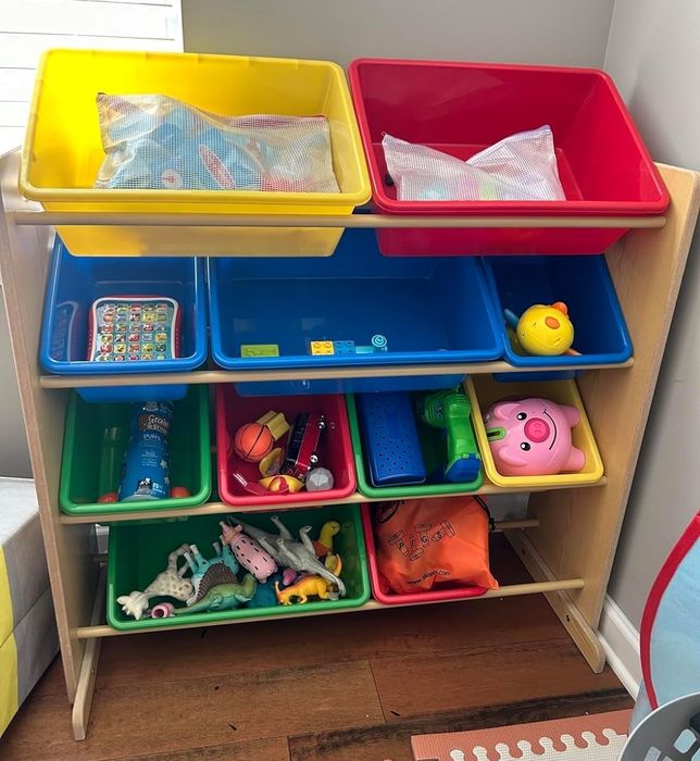 A toy organizer with multiple bins containing toys and children’s items, placed in a playroom