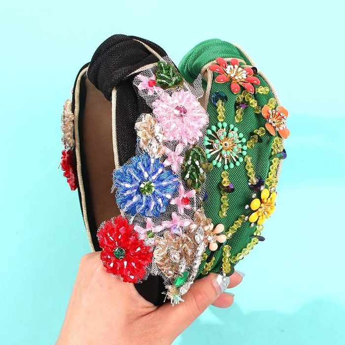 A hand holding black and green headbands with knots on top and oversized beaded flowers on the sides.