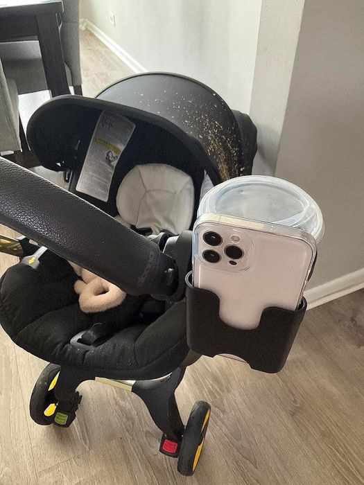 A baby stroller featuring a phone secured in a clear case and a drink in the cup holder, showcasing practical add-ons