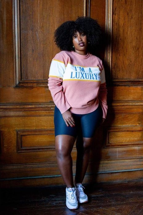A pink sweater featuring a white stripe in the middle with the words 'I'm a luxury' written in blue across it.
