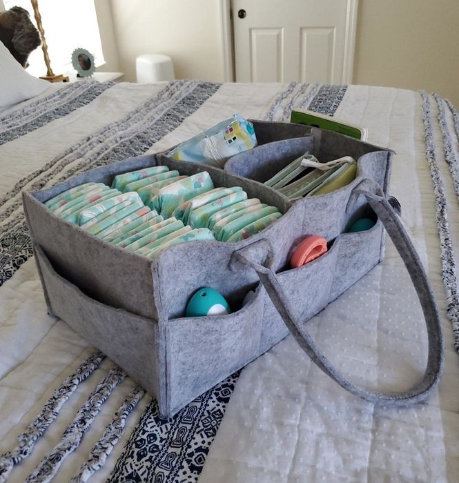 A foldable diaper caddy organizer filled with baby supplies, placed on a bed