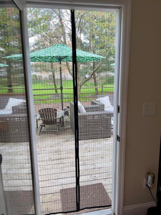 A screened patio door with outdoor furniture and an umbrella visible through the mesh screen