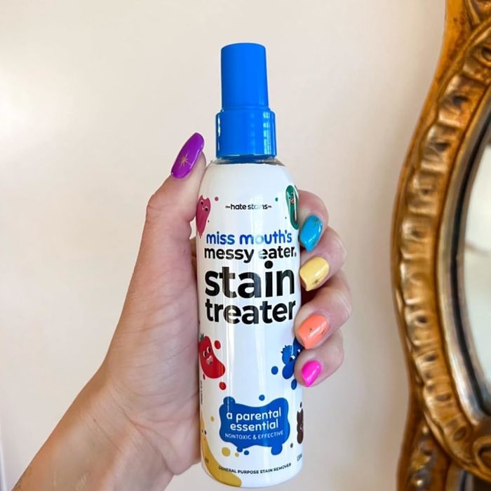 A hand holding a bottle of Miss Mouth's Messy Eater Stain Treater spray