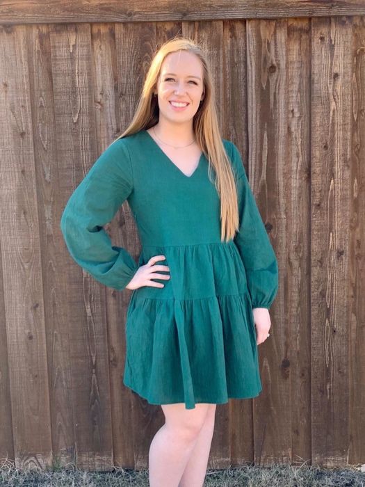 reviewer wearing the green dress standing in front of a wooden fence