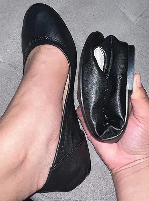 A reviewer is shown wearing one black flat and holding the other, which is folded in half