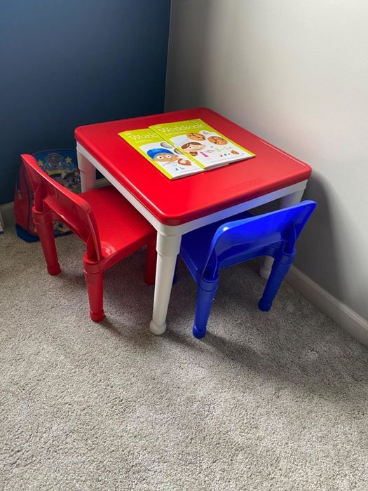 A children's table with a red tabletop, featuring a book about animals, with red and blue chairs accompanying the set.