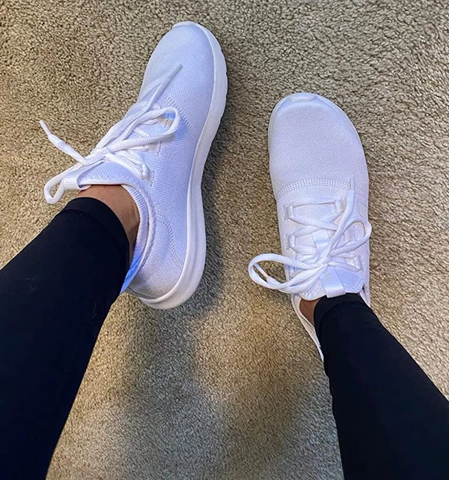 A reviewer is pictured wearing the white Adidas sneakers