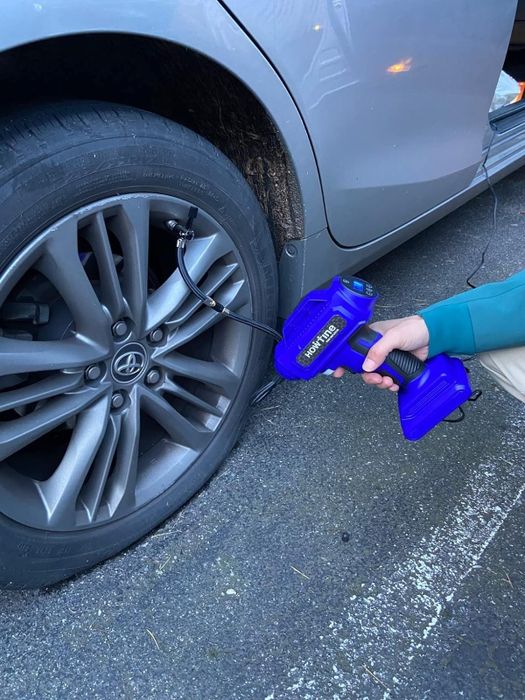 A person using a portable blue air compressor to inflate a car tire. The image is part of an article about useful automotive tools
