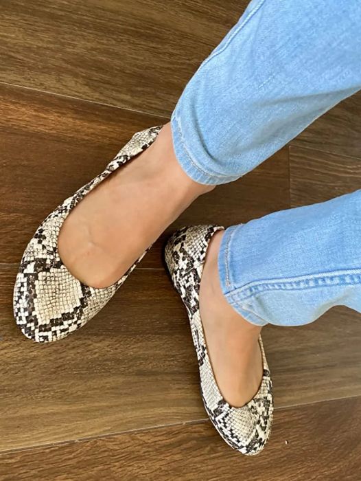 A reviewer is pictured wearing snakeskin flats paired with jeans
