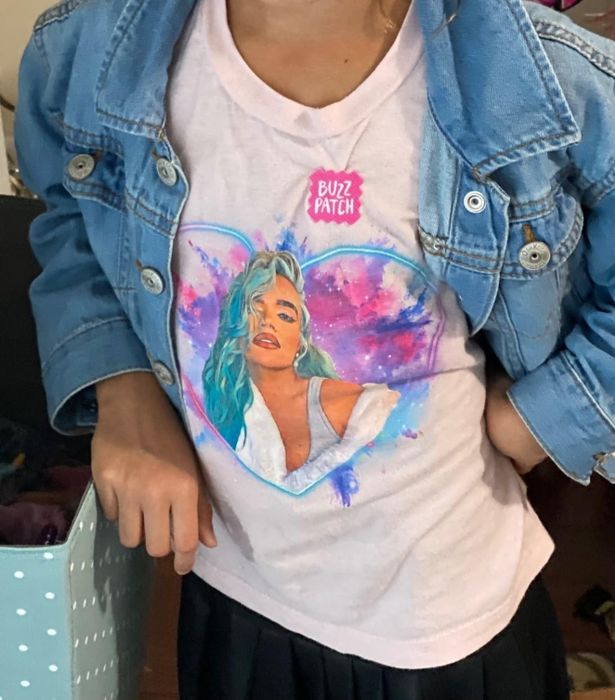 A person is wearing a denim jacket over a t-shirt that features artwork of a woman with teal hair, and the shirt displays the text 