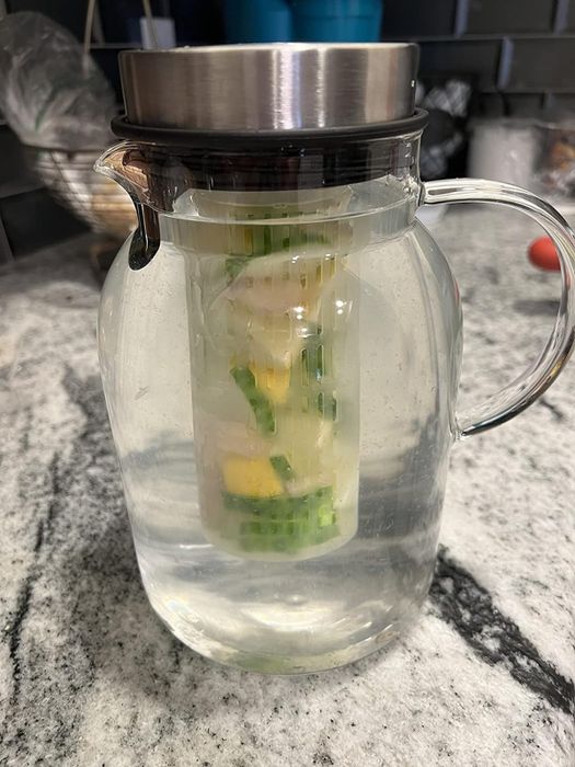 A glass pitcher filled with water, with a filter insert containing cucumber and lemon slices, resting on a kitchen countertop