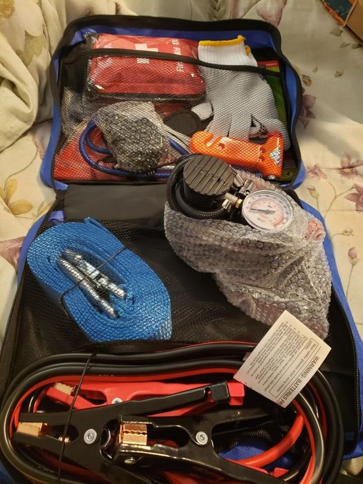 An open emergency car kit containing gloves, jump cables, a tire pressure gauge, and first aid supplies